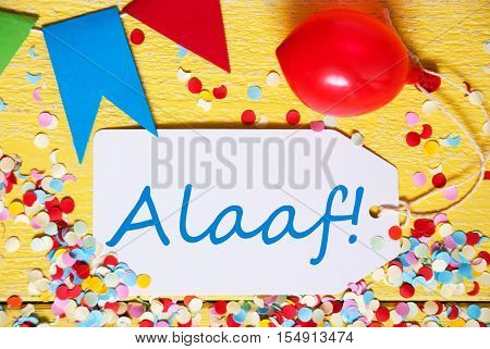 White Label With German Text Alaaf Means Happy Carnival. Close Up Of Party Decoration Like Streamer, Confetti And Balloon. Flat Lay Or Top View. Yellow Wooden Background