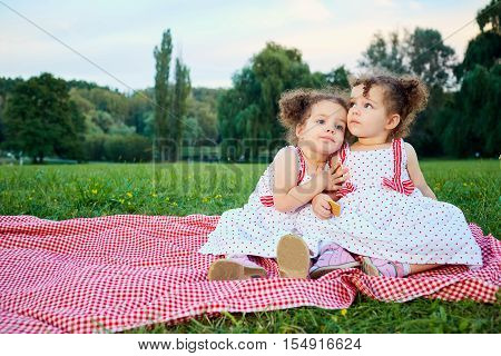 Two sisters twin child in a park outdoors sitting on grass together. Children protection day.
