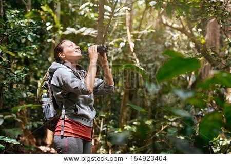 Hiker watching through binoculars wild birds in the tropical jungle. Bird watching tours. Ecotourism concept image travel.