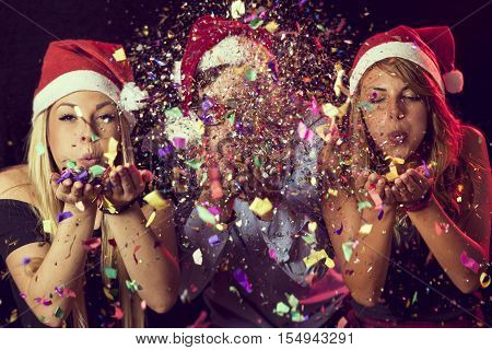 Three young people wearing Santa's hats blowing colorful conffeti at midnight at New Year's Eve party