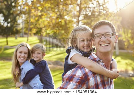 Parents carry their kids piggyback in a park selective focus