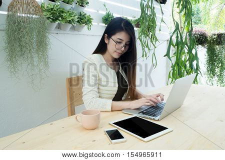 Wood table with Asian woman typing on laptop and blank screen on tablet Smartphone. Asian woman drinking coffee and finding job Concept of business time. Asian woman working at home.