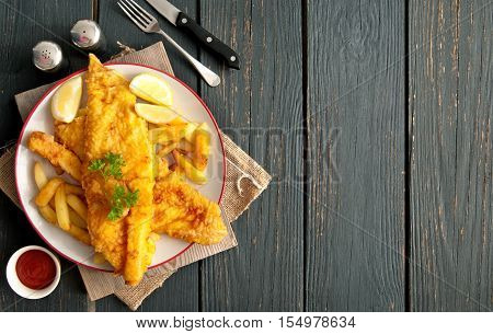 Two pieces of battered fish on a plate with chips on a wooden table with space