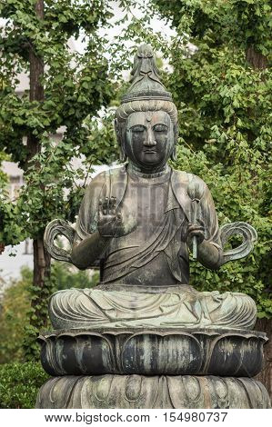 Tokyo Japan - September 26 2016: Closeup of bronze statue of Seishi Bosatsu attendant of Amida Buddha sitting on lotus pedestal in garden at Senso-ji Buddhist Temple. Green foliage.