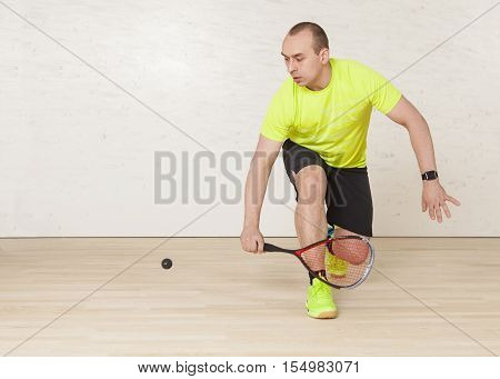 Young Caucasian man in a yellow T-shirt playing squash. Horizontal color image.