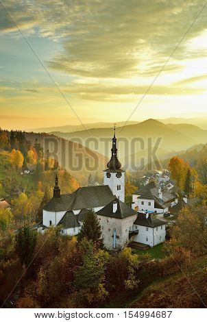Fall in Slovakia. Old mining village. Historic church in Spania dolina. Autumn colored trees at sunset.