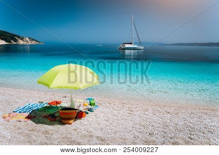 Idyllic White Beach With Umbrella On Lazy Summer Day. Sailing Boat At Anchor In Calm Crystal Clear B