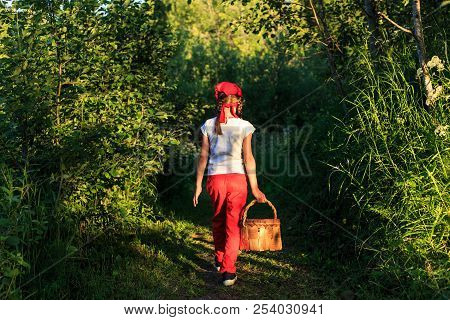 Young Girl Walking On A Path Through Green Woods Carrying A Birchbark Basket