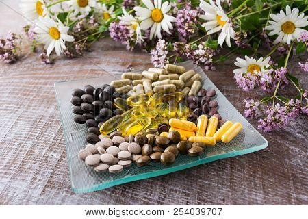 Ayurvedic Herbal Pills On The Glass Plate With Wild Chamomile And Tansy Flowers. Healthy Life Concep