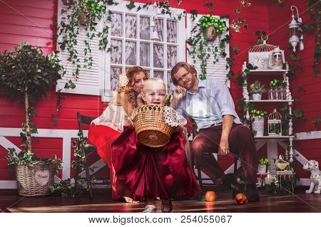 Happy Caucasian Family With At The Red House Patio. Baby Girl Holding A Basket And Runnning
