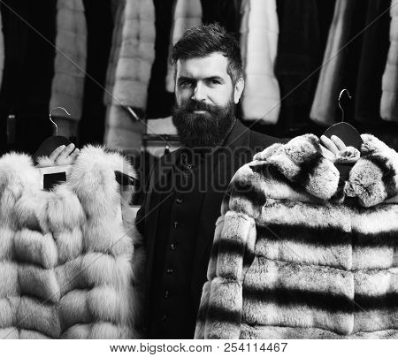 Guy With Strict Face Shows Two Fur Coats.