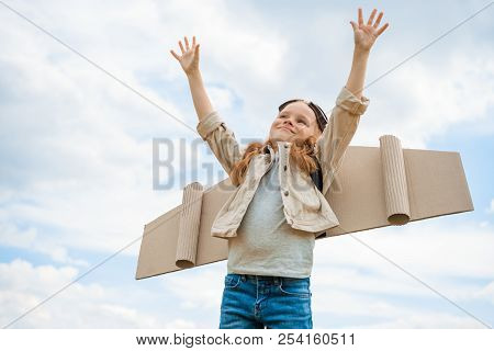 Low Angle View Of Child With Paper Plane Wings And Protective Eyeglasses With Outstretched Arms Agai