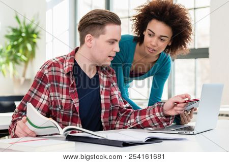 Two young students browsing internet for online useful up-to-date information while writing together an assignment in the interior of a modern university