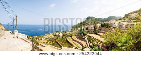 Panoramic Shot Of Typical Village And Landscape Against Blue Sea And Sky On Island Of Mallorca, Spai