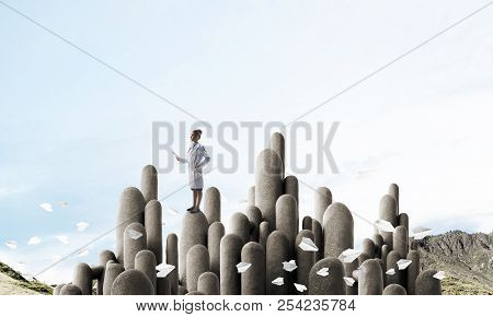 Young Female Doctor With Folder In Hands Satnding On Stone Column