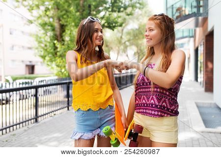 friendship, leisure and gesture concept - happy teenage girls or friends with skateboards on city street in summer making fist bump