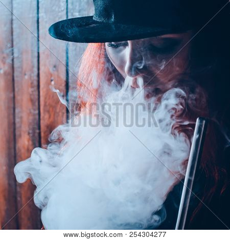 Red-haired Sexy Girl Dressed In Swimsuit And Cap Smoking A Hookah. Toned Image. Concept Of Pleasant 