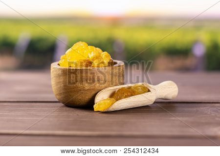 Lot Of Whole Dry Golden Raisins Sultana Variety Scoop With Wooden Bowl With Vineyard In Background
