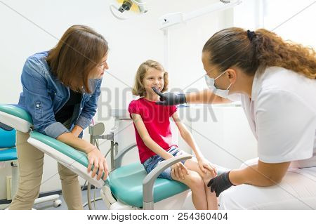 Mother And Little Daughter Visiting Dentist At Dental Clinics. Orthodontist Puts On, Corrects The De