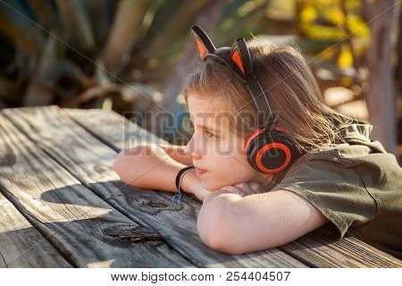 A Young, Blond Girl Sits With Her Chin On Her Hands At A Picnic Table In The Desert With Late Aftern