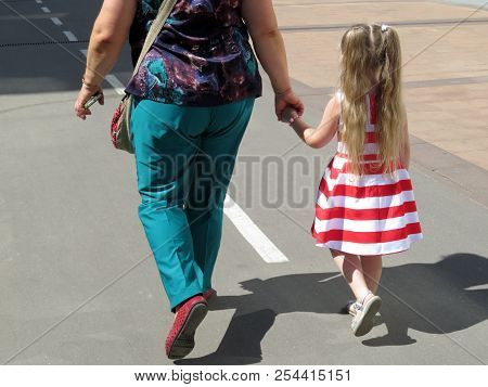 Woman Leads By The Hand A Little Girl In A Summer Dress. Concept For Grandmother And Granddaughter, 