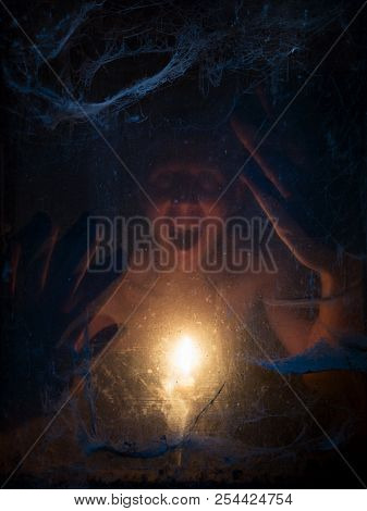 Halloween celebration background. Face in darkness and in the light of a candle. Old terrible cobweb