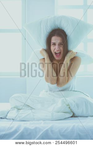 Young caucasian woman covering her head and ears with pillows.