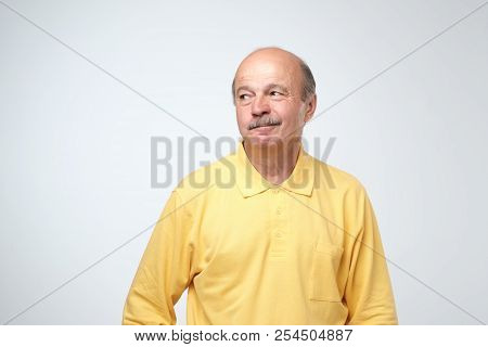 Mature Old Attractive Man In Yellow Shirt With Skeptic Look, Raises Eyebrow In Bewilderment, Has Som