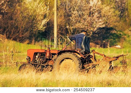 A Tractor Driver Plowing Soil In Autumn To Sow Winter Wheat. Side View Of A Tractor Driver On Tracto