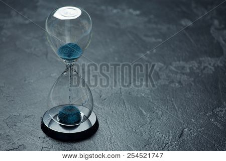 Image of hourglass with blue sand on black background