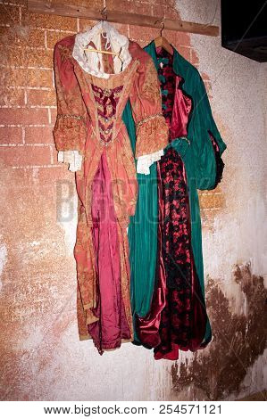 Old Venetian Style Feminine Dresses Of Green And Red Color On The Coathanger In The Dresser. Brick W