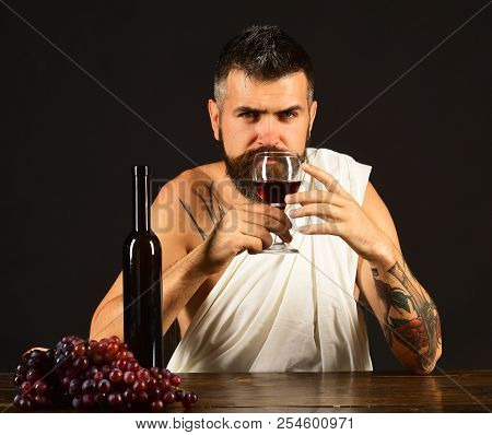 Sommelier Smells Drink. God Bacchus With Serious Face Wearing White Cloth Sits By Wine Bottle And Gr