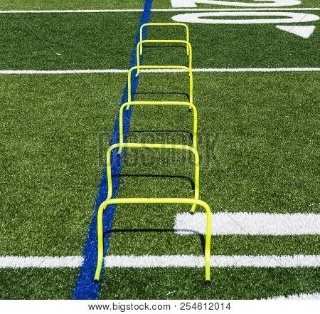 Six Yellow Mini Hurdles Are Set Up On A Green Turf Field As Part Of A Teams Speed And Agility Practi