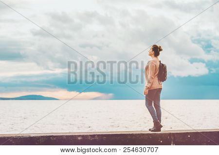 Outdoor Portrait Of Young Woman Resting By The Lake On A Fresh Cold Day, Wearing Warm Pullover And B