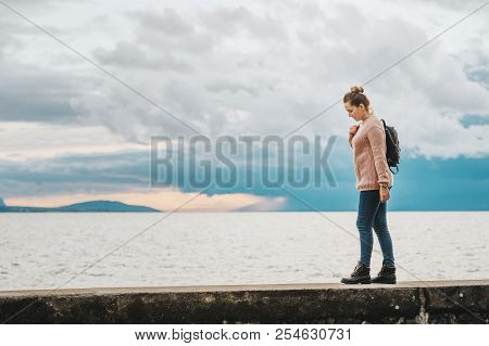 Outdoor Portrait Of Young Woman Resting By The Lake On A Fresh Cold Day, Wearing Warm Pullover And B