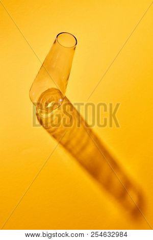 A transparent glass flask empty lies on a yellow paper background with abstract shadows, place for text. Laboratory chemical tools. Laboratory concept.