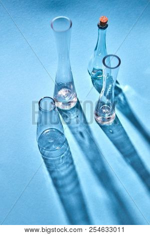 Empty glasses with diagonal long shadows on light blue paper background, space for text. Test glass flask in research laboratory.