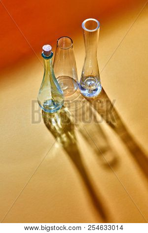Long diagonal shadows from three glass flasks empty on a duotone yellow paper background with place under text. The Chemistry Lab. Various glass chemistry lab equipment