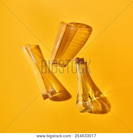 Three empty glass bottles lie on a yellow background with shadows and reflection, place for text. Top view. Test glass flask in research laboratory. Science and medical background.