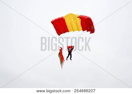 A Parachutist With A Bright Multicolored Parachute Flies Across The Sky With The Flag Of The Republi