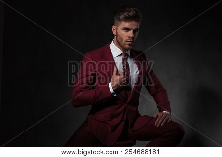 portrait of gentleman holding his grena suit collar looking to side while sitting on grey background