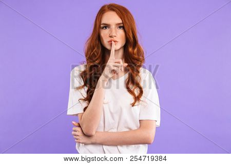 Portrait of a serious young girl standing isolated over violet background, showing silence gesture