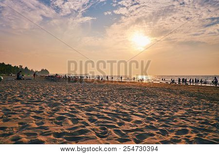 The Evening On The Cozy Sand Beach With Holidaymakers, Walking Along The Shore And Enjoying The Weat