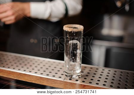 Cocktail Glass With An Ice Cube And Sugar Edge On The Bar Counter On The Blurred Background Of Barte