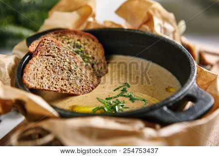 Mushroom Cream Soup with Herbs and Spices in Metal Bowler on Rustic Wooden Background. Homemade Creamy Soup Made of Champignons, Boletus or Ceps with Rye Bread Toasts, Greens and Butter