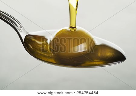 Bottle Of Virgin Olive Oil Pouring To The Spoon Close Up