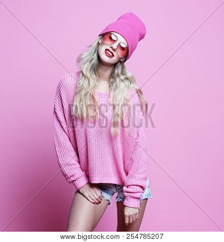 Stylish fashion portrait of trendy casual young woman in pink pulover and hat, posing over pink background.