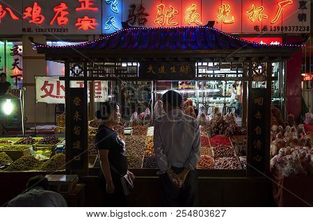 Dunhuang, China - August 7, 2012: A Vendor And A Costumer In Front Of A Food Stall At A Street Marke