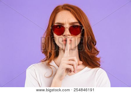 Portrait of a serious young girl standing isolated over violet background, showing silence gesture