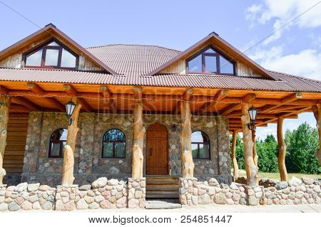 A Large Wooden Hut House In The Woods Of Logs Of Planks And Stone With Columns Of Tree Trunks With A